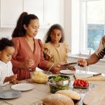 A family shares a joyful meal preparation in a bright, modern kitchen setting.